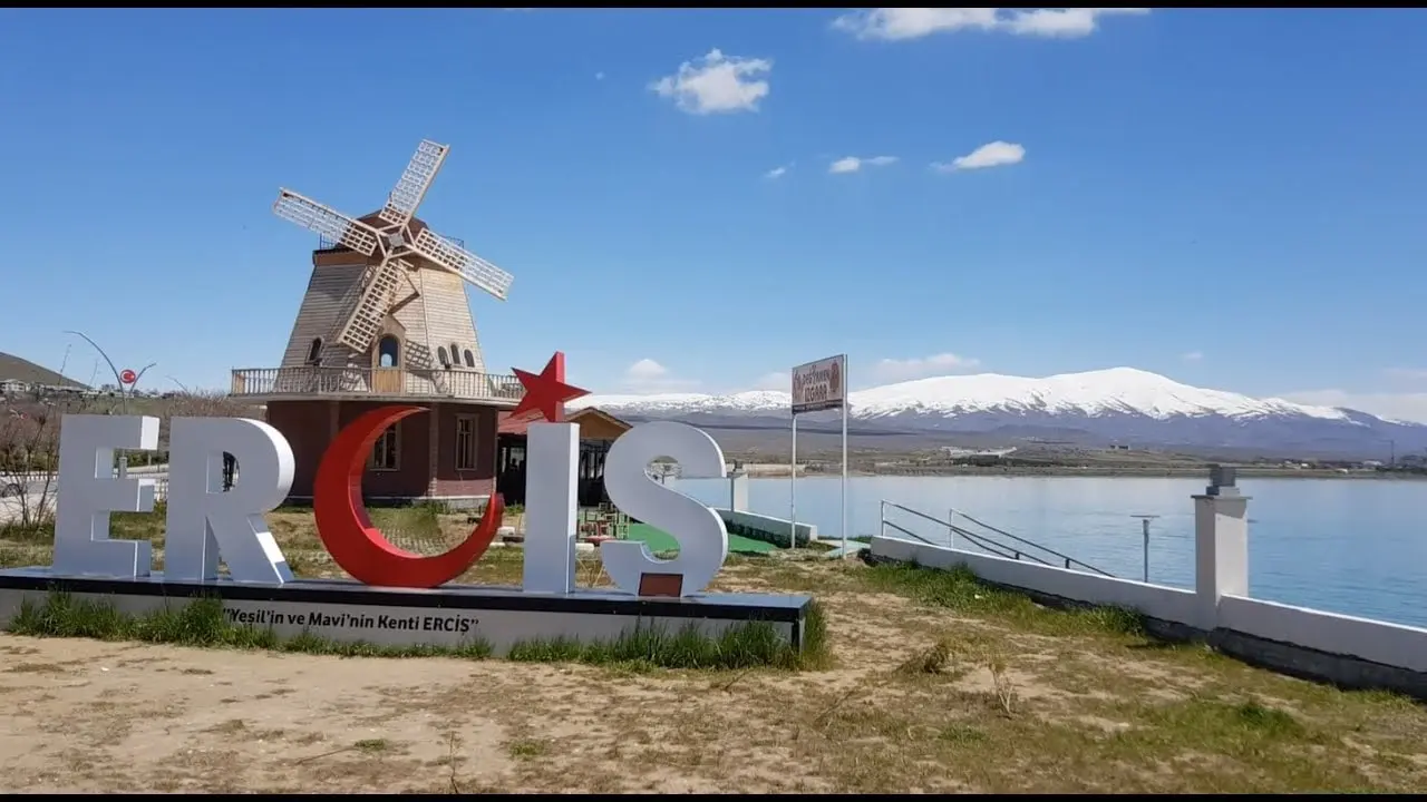 An Erciş sign and decorative windmill beside the lake, with snowy mountains beyond