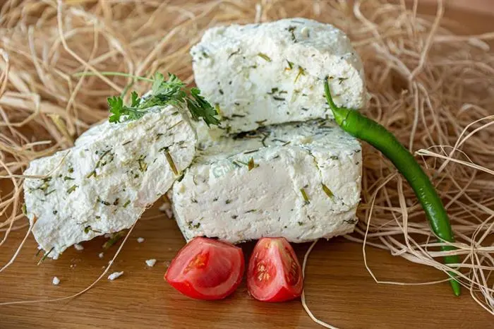 Ahşap üzerinde otlu peynir parçaları, iki domates dilimi ve yeşil biber.