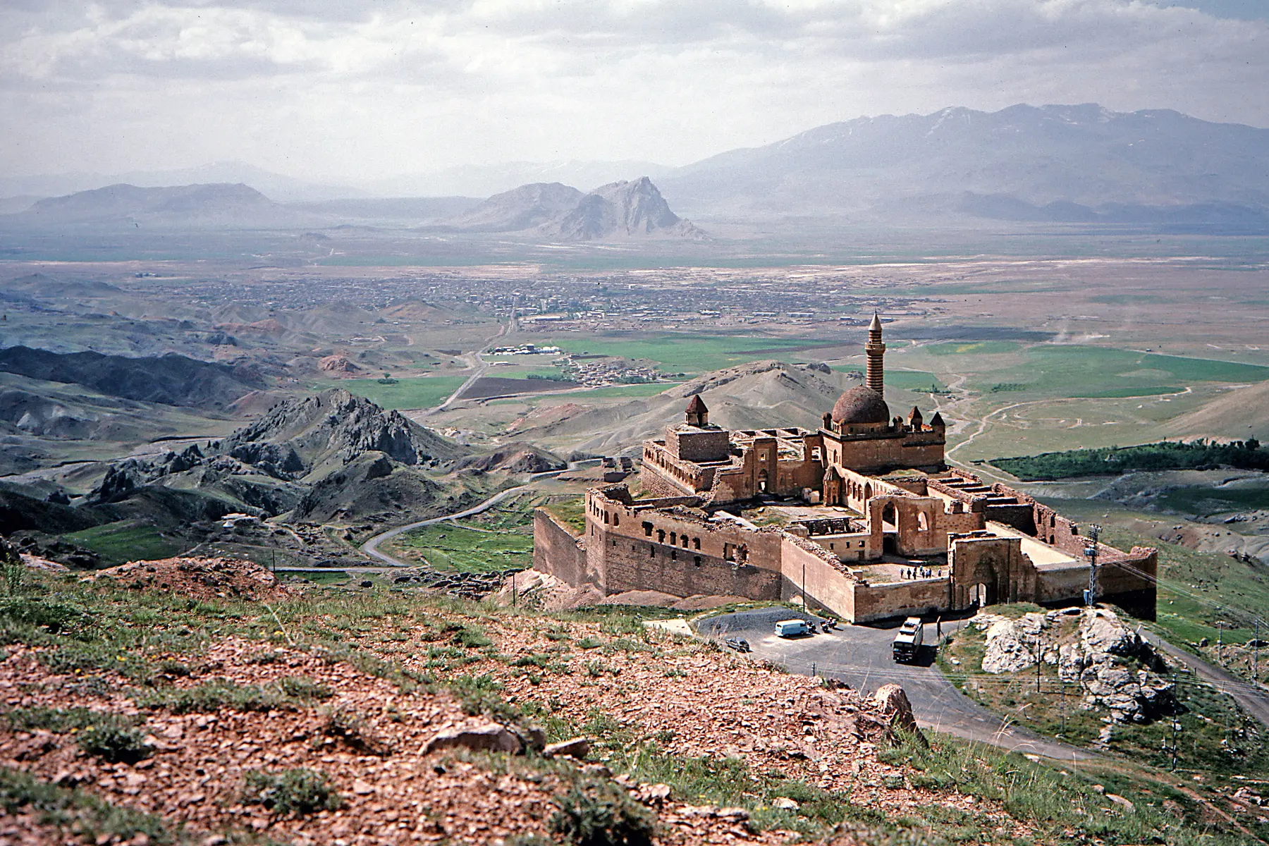 The stone walls, dome and minaret of Ishak Pasha Palace on a rocky hillside above the broad Doğubayazıt plain.
